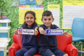 two elementary students holding signs that say Follow us on Instagram and Follow Us on Facebook