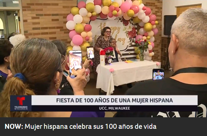 People look on in celebration as a woman and her daughter pose for a photo underneath a pink and yellow balloon arch.