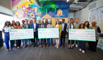 Three groups of people stand together. Each group holds a large check.